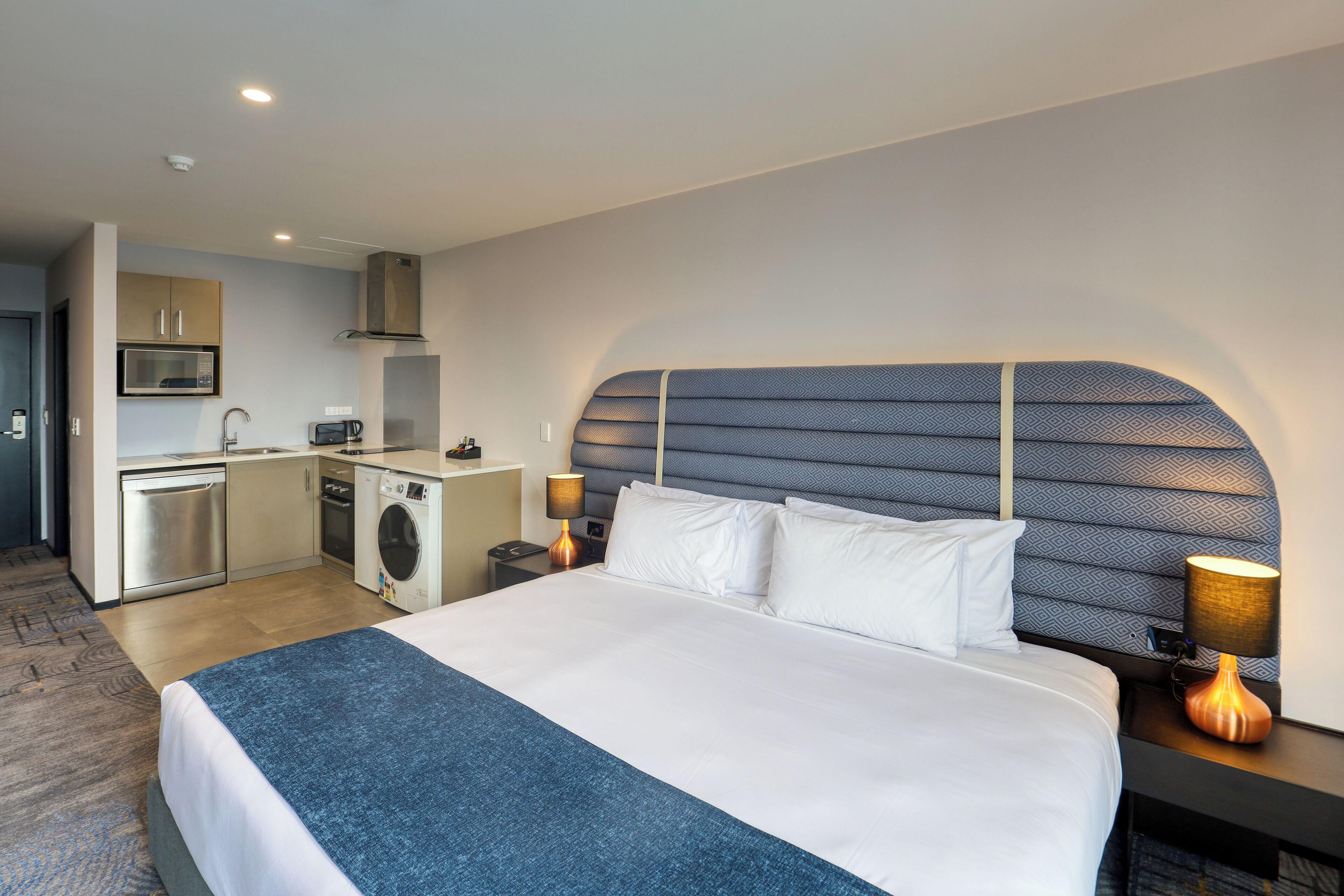 Ein Hotelzimmer mit einem großen Bett, einem Kopfteil mit geometrischem Muster, einer integrierten Waschmaschine, einer Mikrowelle und einem Waschbecken.