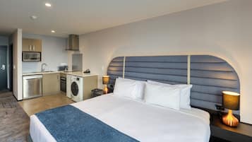 Ein Hotelzimmer mit einem großen Bett, einem Kopfteil mit geometrischem Muster, einer integrierten Waschmaschine, einer Mikrowelle und einem Waschbecken.