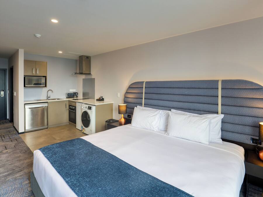 Ein Hotelzimmer mit einem großen Bett, einem Kopfteil mit geometrischem Muster, einer integrierten Waschmaschine, einer Mikrowelle und einem Waschbecken.