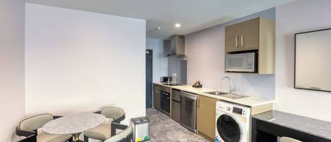 A compact kitchen with a microwave, sink, and washing machine. There is a small dining table with chairs.