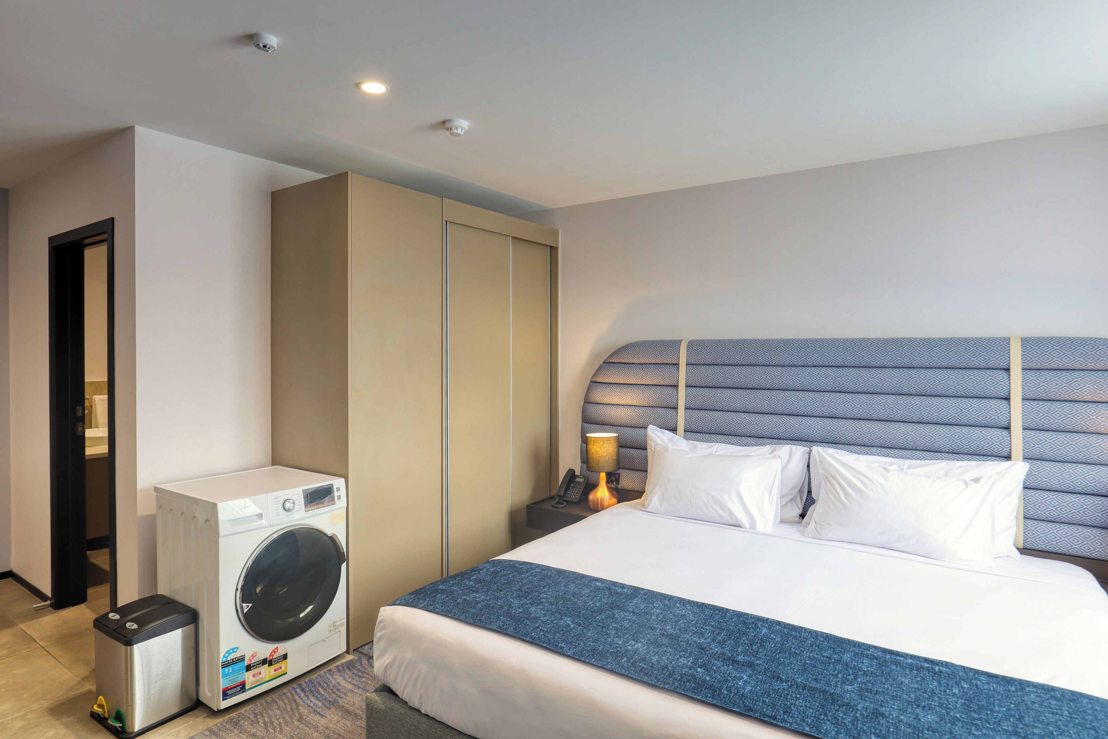 A hotel room with a bed, a washing machine, a nightstand, and a wardrobe.