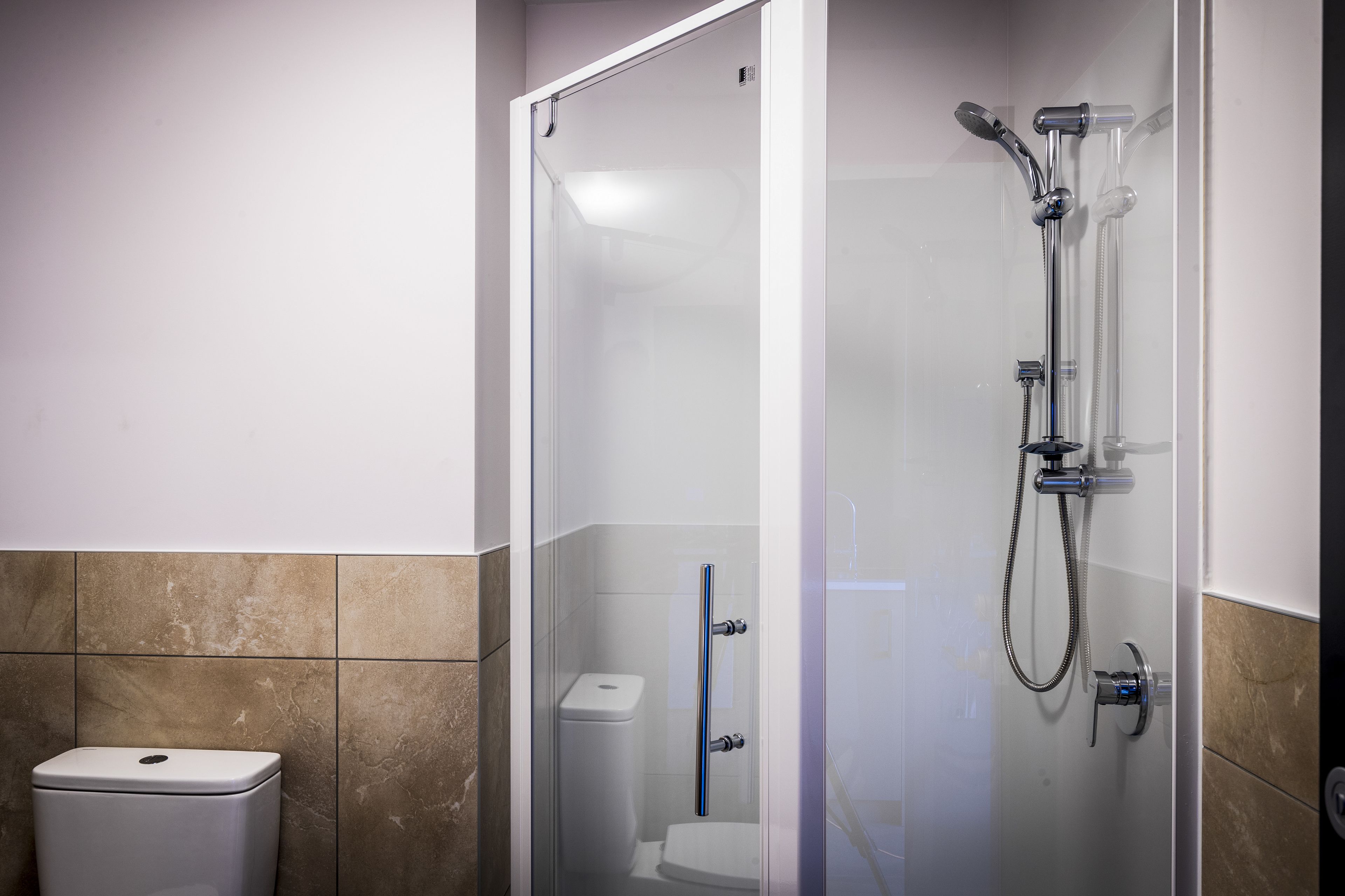 A glass-enclosed shower with a handheld showerhead and a wall-mounted faucet.