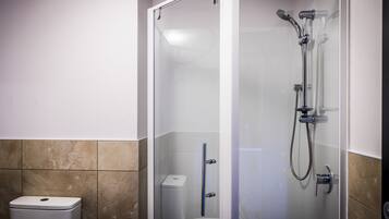 A glass-enclosed shower with a handheld showerhead and a wall-mounted faucet.