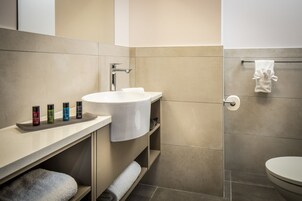Un baño moderno con un lavamanos blanco, baldosas color beige y un perchero para toallas.