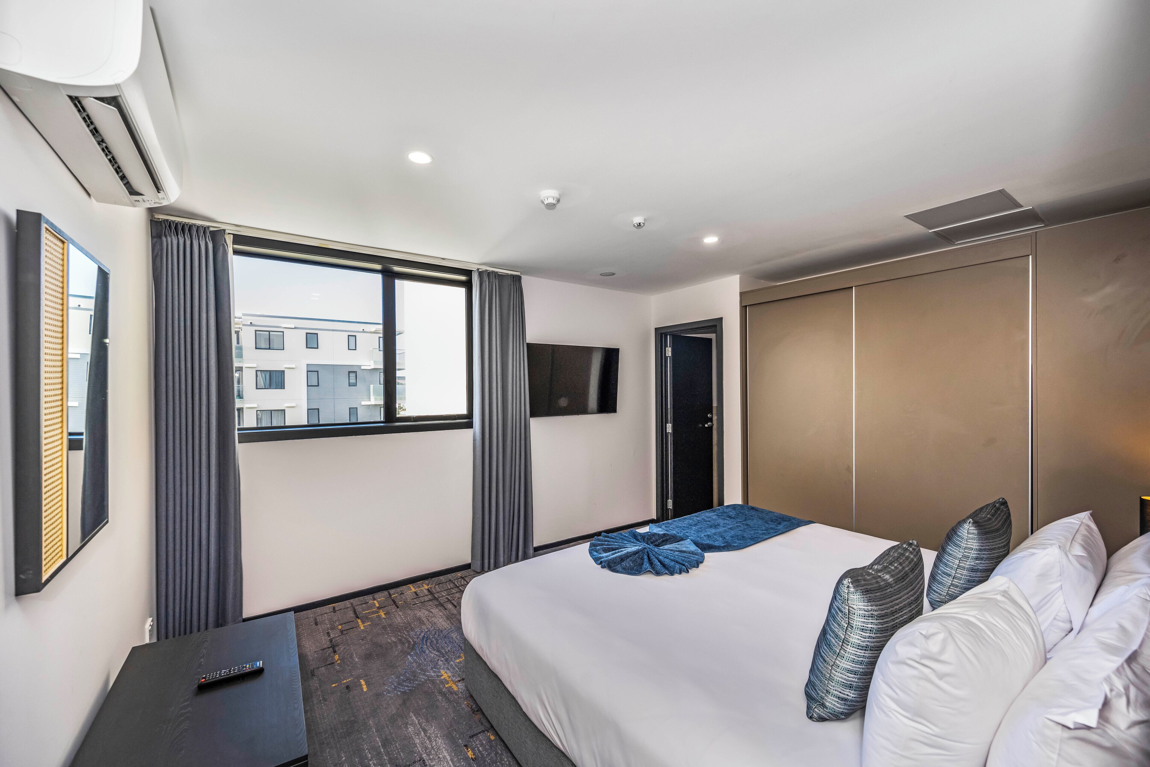 Une chambre d’hôtel avec un grand lit, un téléviseur fixé au mur, une armoire et une fenêtre avec des rideaux.