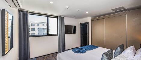 Une chambre d’hôtel avec un grand lit, un téléviseur fixé au mur, une armoire et une fenêtre avec des rideaux.