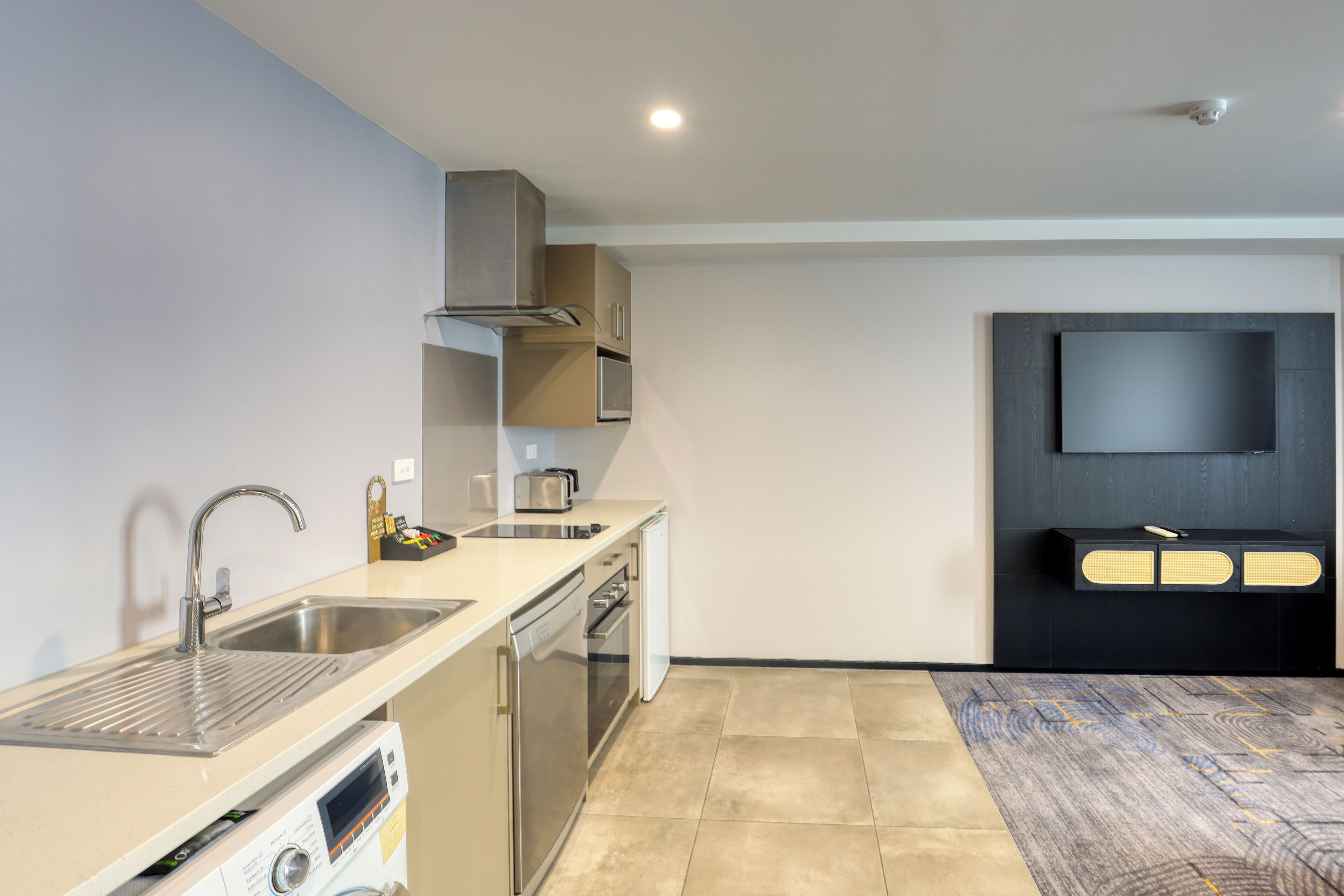 A modern kitchen with stainless steel appliances, a built-in dishwasher, and a flat-screen TV mounted on the wall.