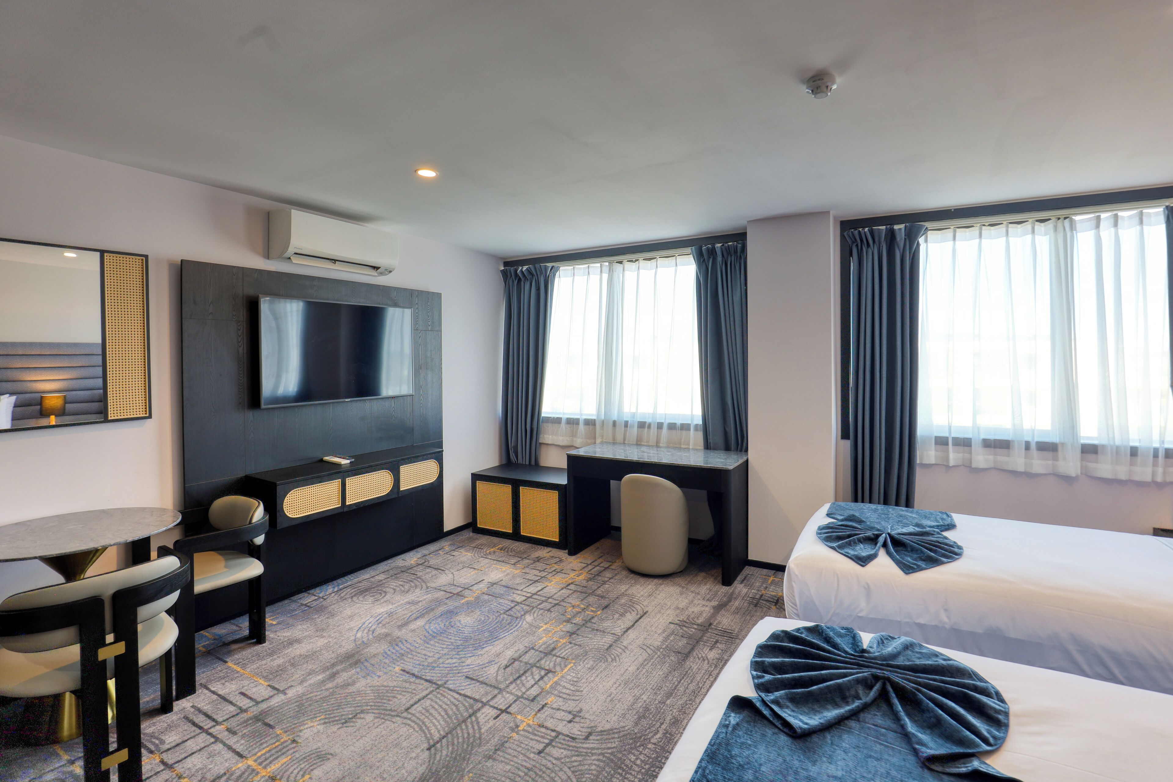 A hotel room with a bed, a desk, a chair, a TV, and a window with curtains.