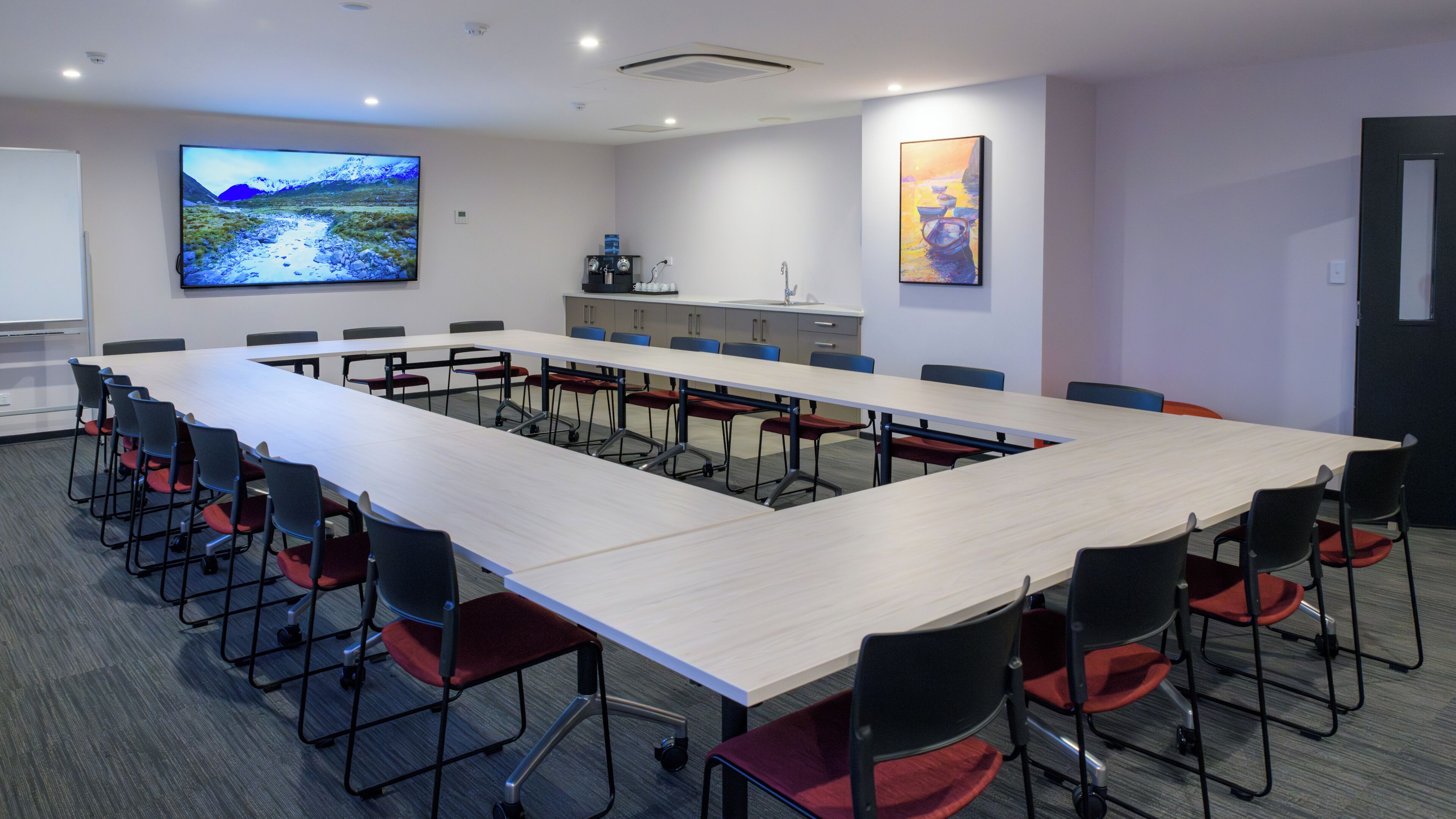 Ein Konferenzraum mit langem Tisch, Stühlen, einer Projektionsleinwand und Kunstwerken an den Wänden.