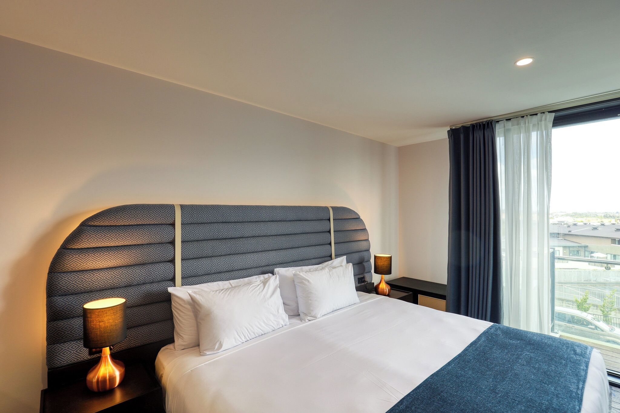 Une chambre d’hôtel avec un grand lit, deux tables de chevet et une vue sur la ville par la fenêtre.