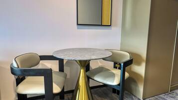 A small, round table with a metallic base, two chairs with cushioned seats, and a wall-mounted mirror with a decorative panel.
