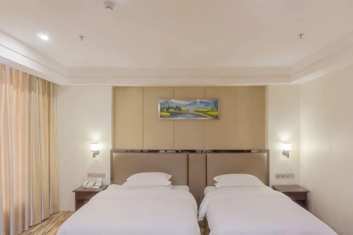 Una habitación de hotel con dos camas, un cuadro en la pared y lámparas de noche.