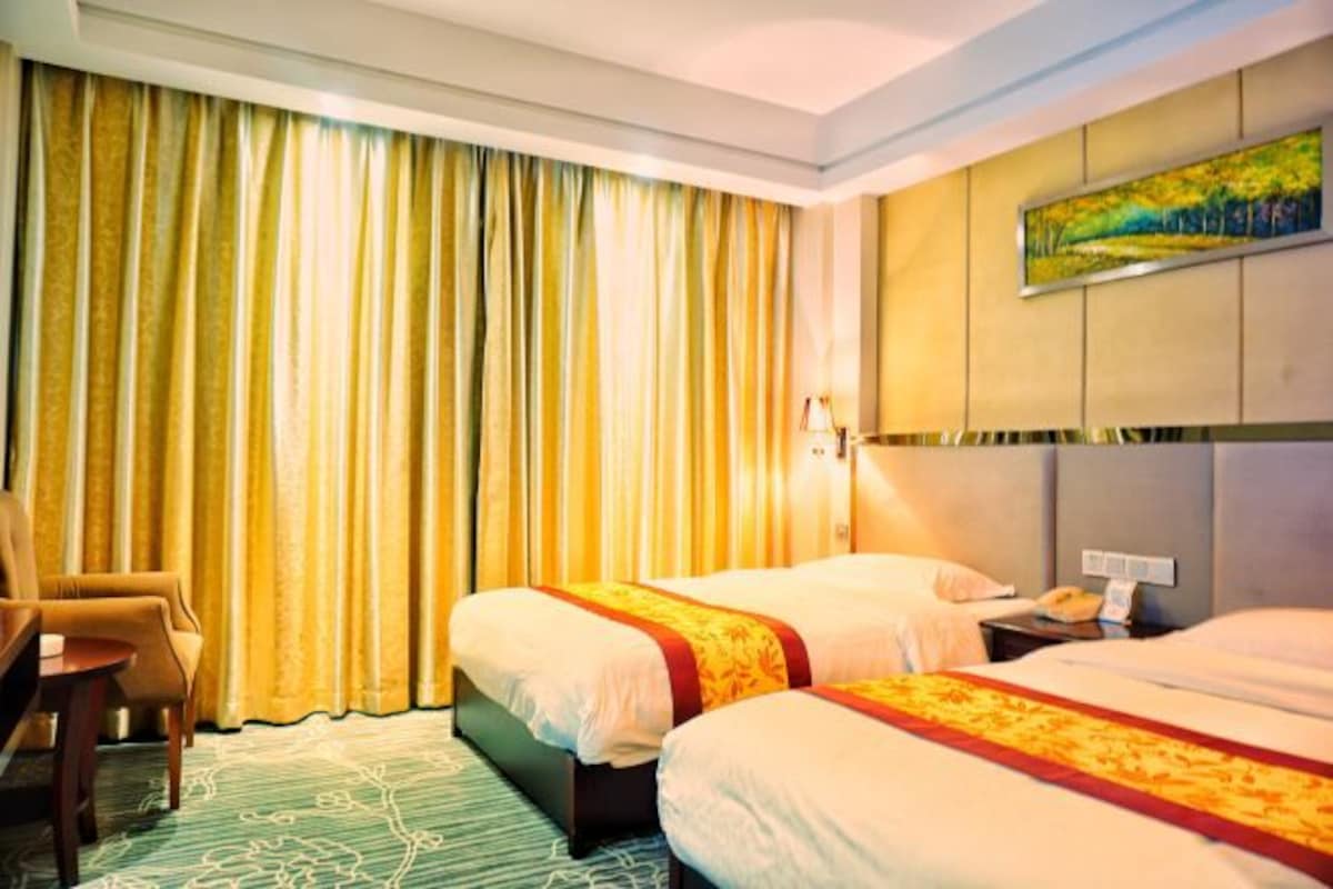Habitación de hotel con dos camas, una silla, un cuadro en la pared y una ventana con cortinas.