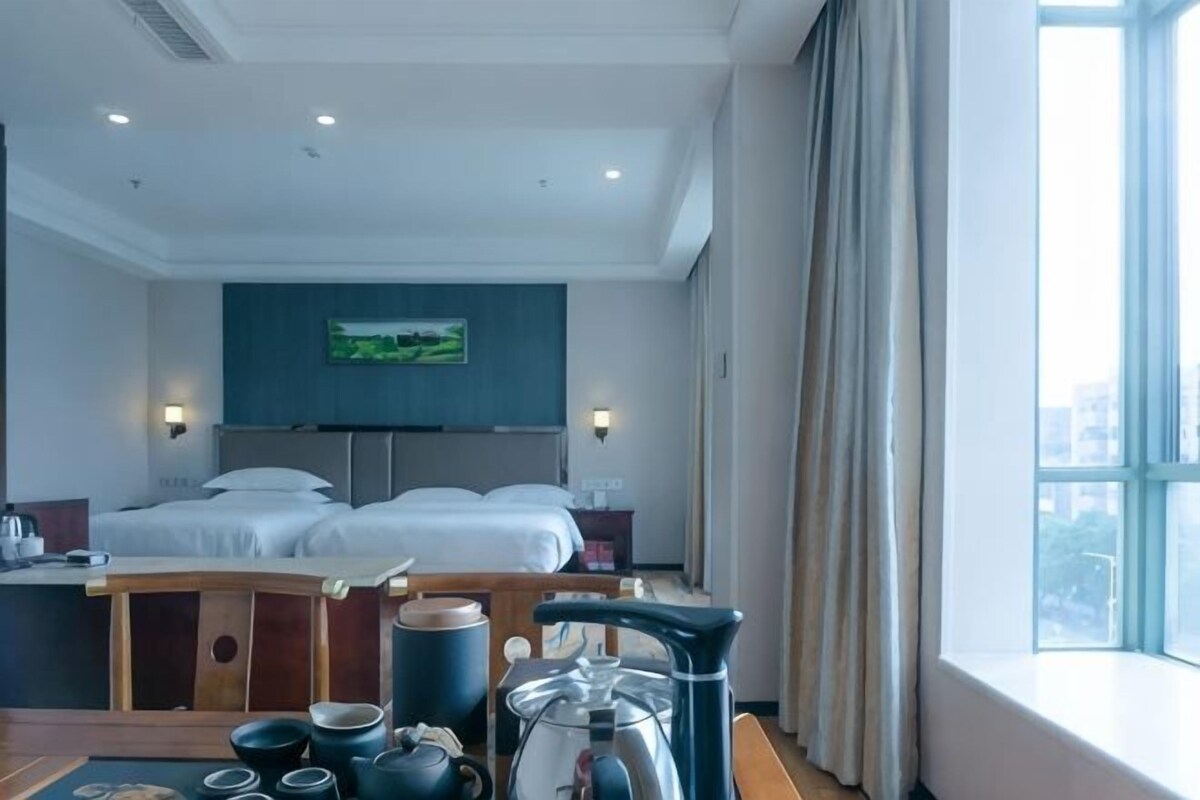 A hotel room with a bed, a desk with a kettle, cups, and a teapot.