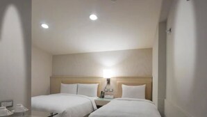 Una habitación de hotel con dos camas individuales, una mesita de noche, una lámpara y un panel de vidrio.