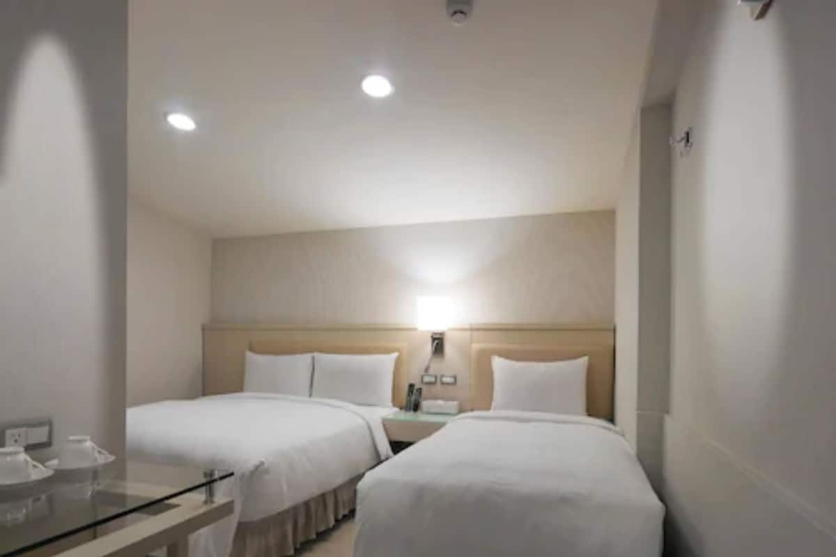 A hotel room with two single beds, a bedside table, a lamp, and a glass partition.