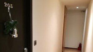 Un pasillo estrecho y bien iluminado, con piso de madera y una puerta oscura con placa de identificación.