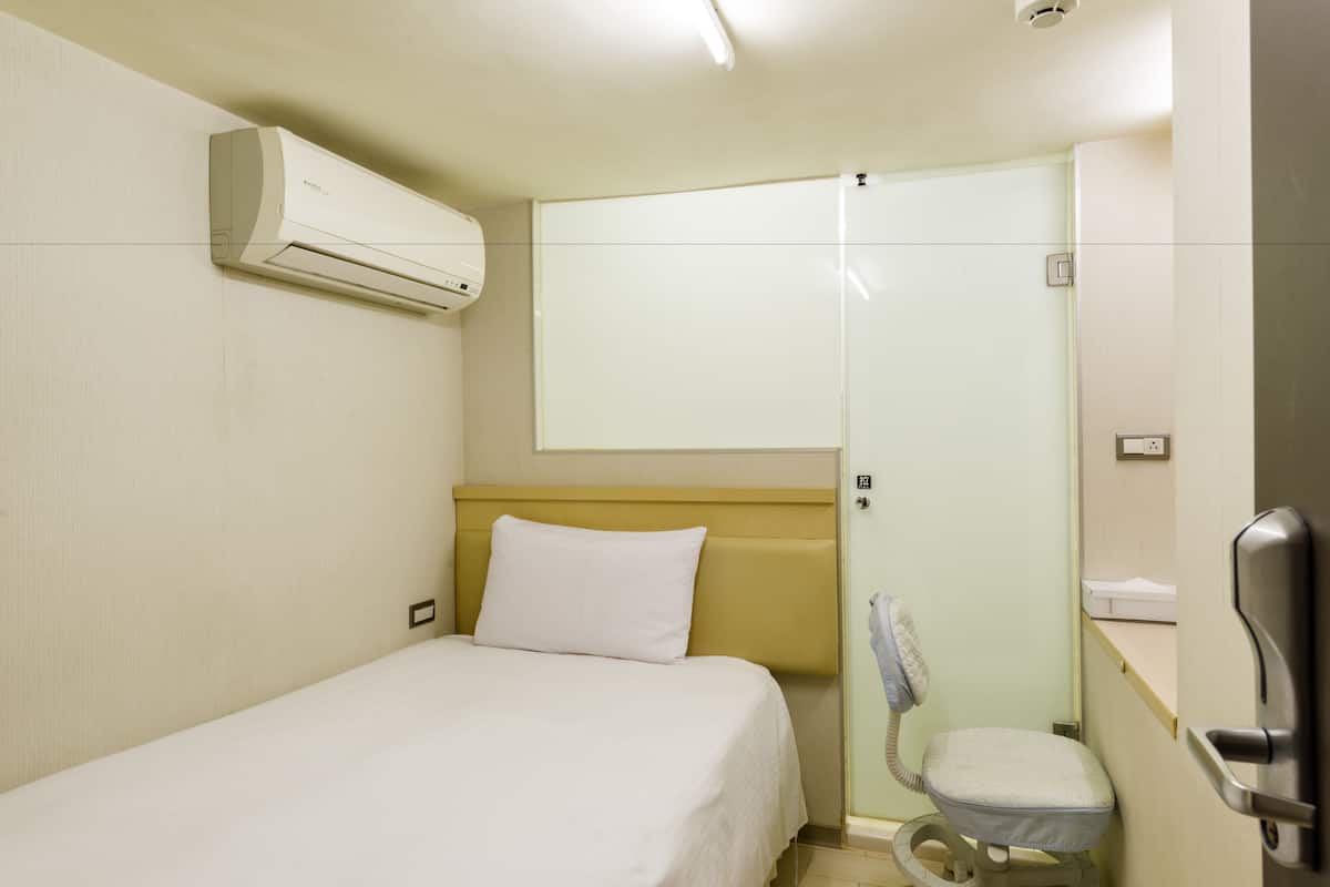A hotel room with a bed, a toilet, a shower, and a wall-mounted air conditioner.