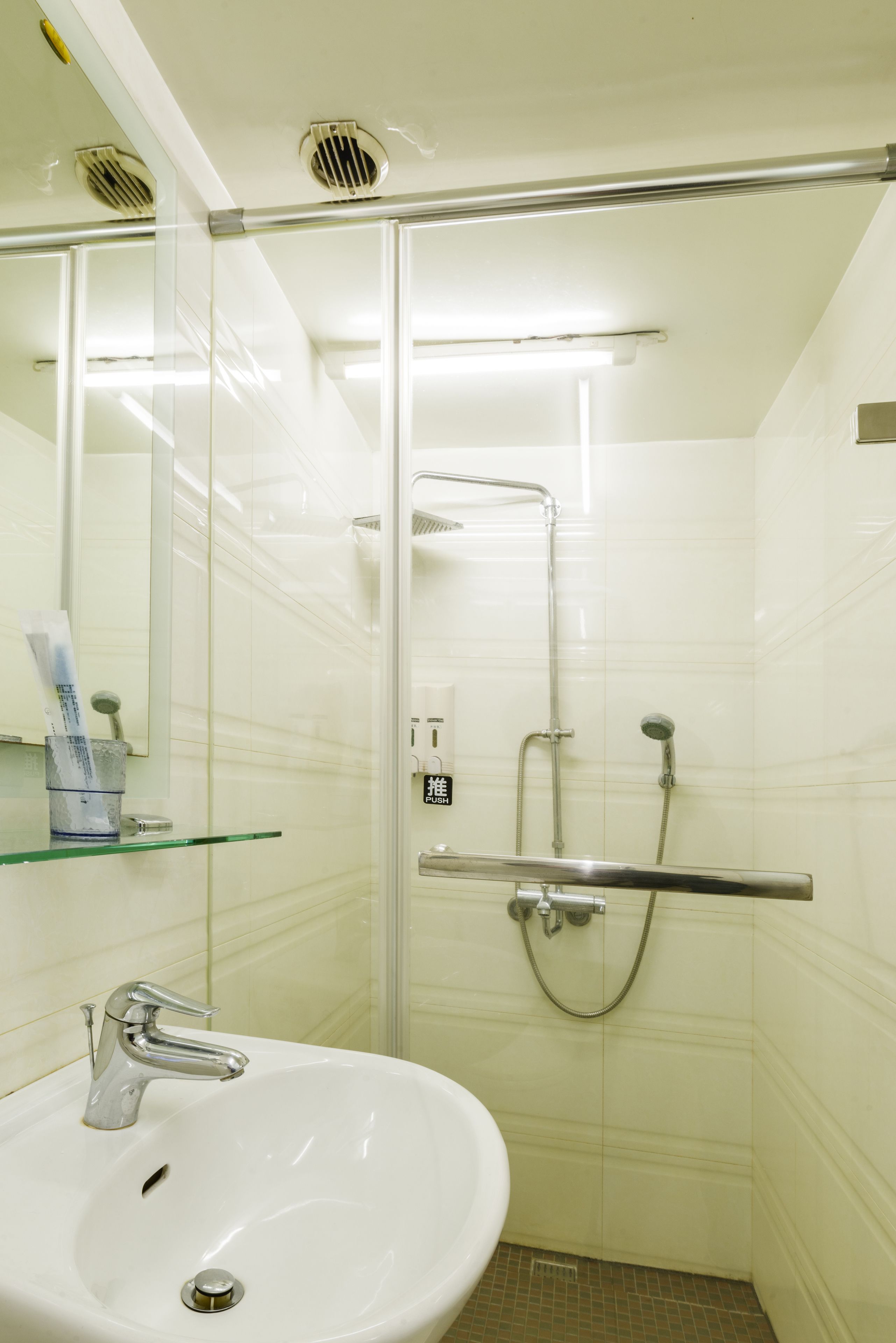 Un baño con un lavamanos blanco, cabina de ducha con mampara de vidrio y un espejo.