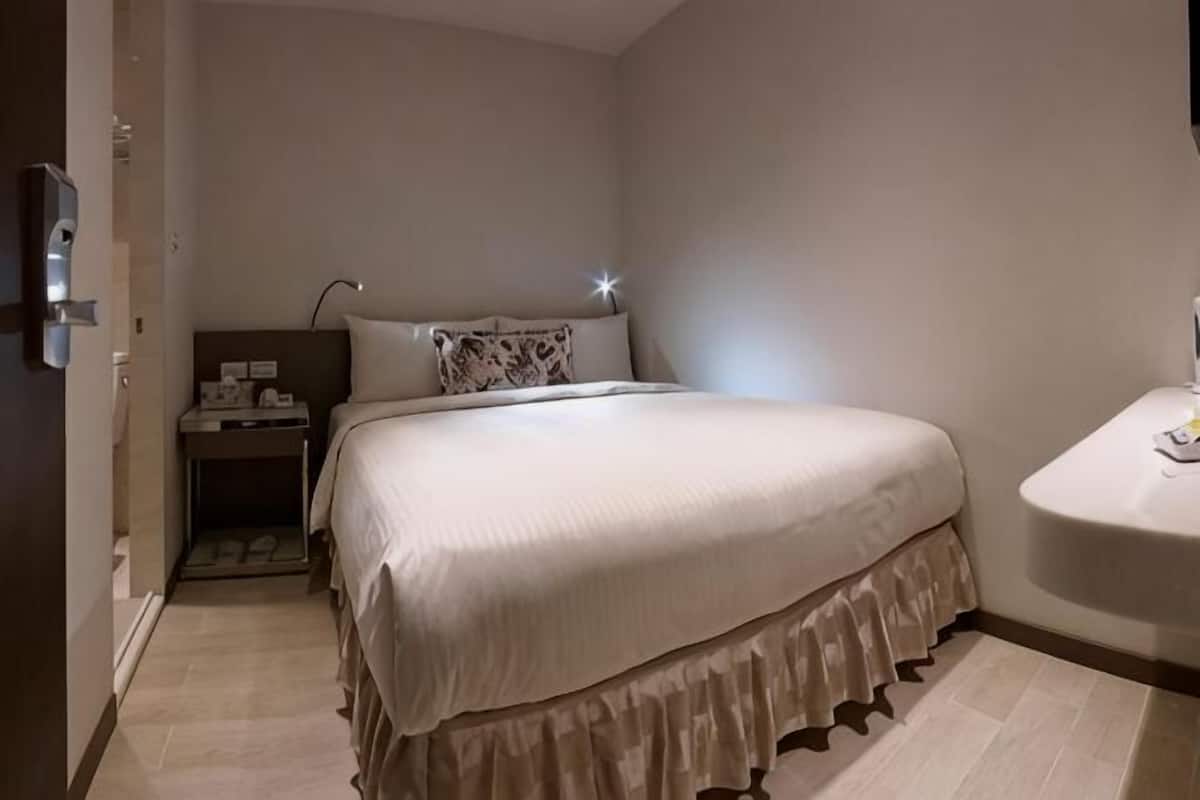 A bedroom with a bed, bedside table, lamp, and a small bathroom area.