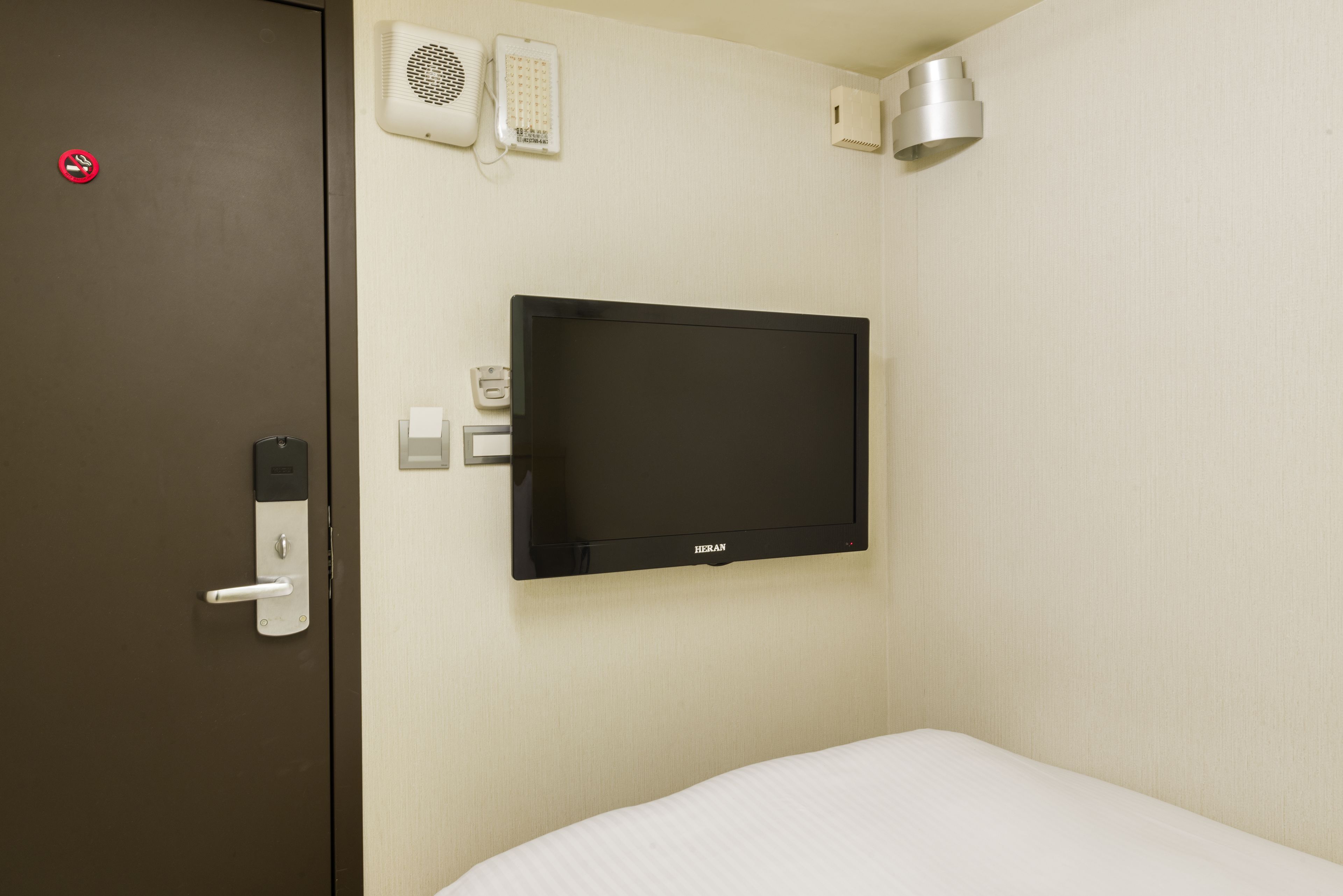 A hotel room with a bed, a television mounted on the wall, a door with a handle, and a wall-mounted phone.