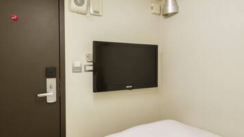 A hotel room with a bed, a television mounted on the wall, a door with a handle, and a wall-mounted phone.