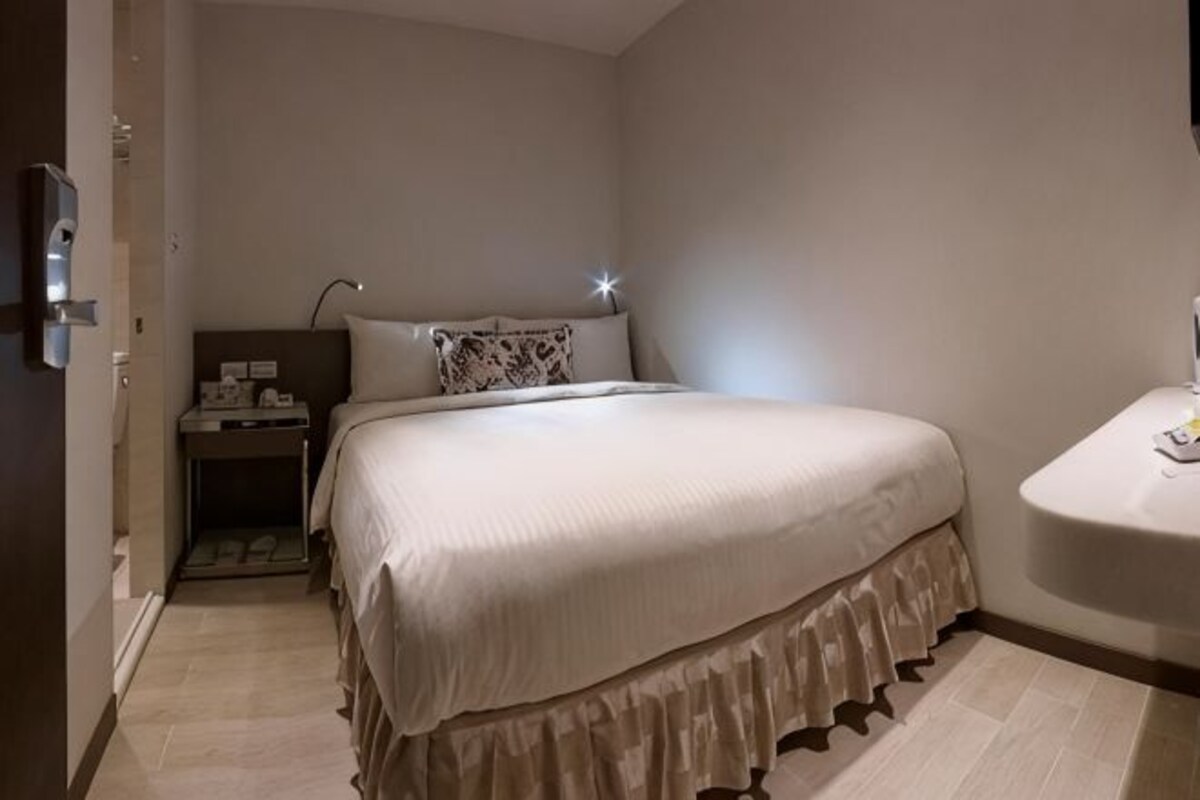 A bedroom with a bed, bedside table, lamp, and a small bathroom area.