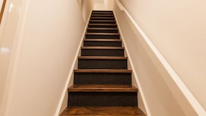 A staircase with wooden steps and a handrail, leading upwards in a narrow hallway with white walls. - Puur Geluk (Groningen)