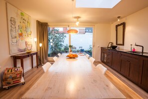 A spacious dining area with a large wooden table, white chairs, a view through a glass door to the outdoors, a pendant light, and a wall-mounted mirror. - Puur Geluk (Groningen)
