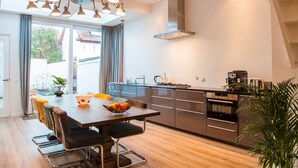 Een moderne keuken met een centraal eiland, roestvrijstalen apparatuur en een eethoek met een grote tafel en stoelen.