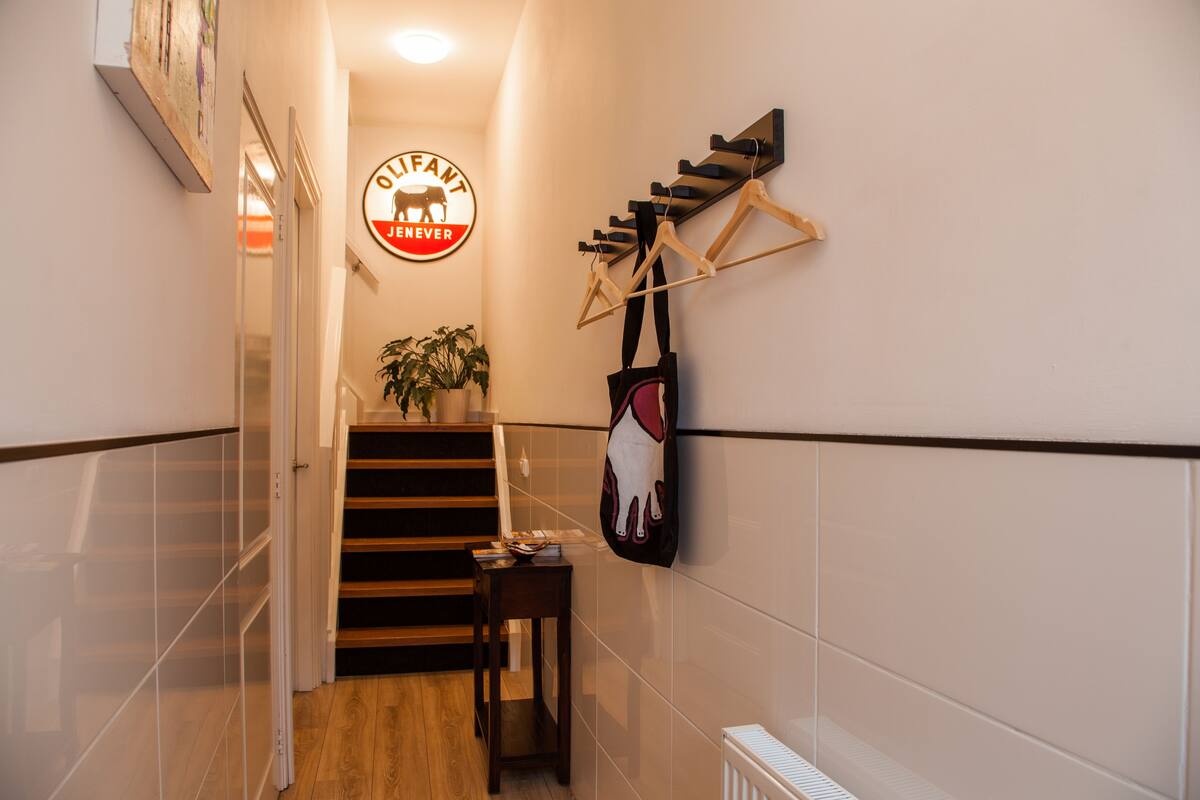 A hallway with a staircase, a coat rack, and a sign that reads "OLIFANT JENEVRE".