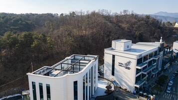 A modern hotel with a glass-roofed structure, a prominent logo, and a view of a forested hillside.