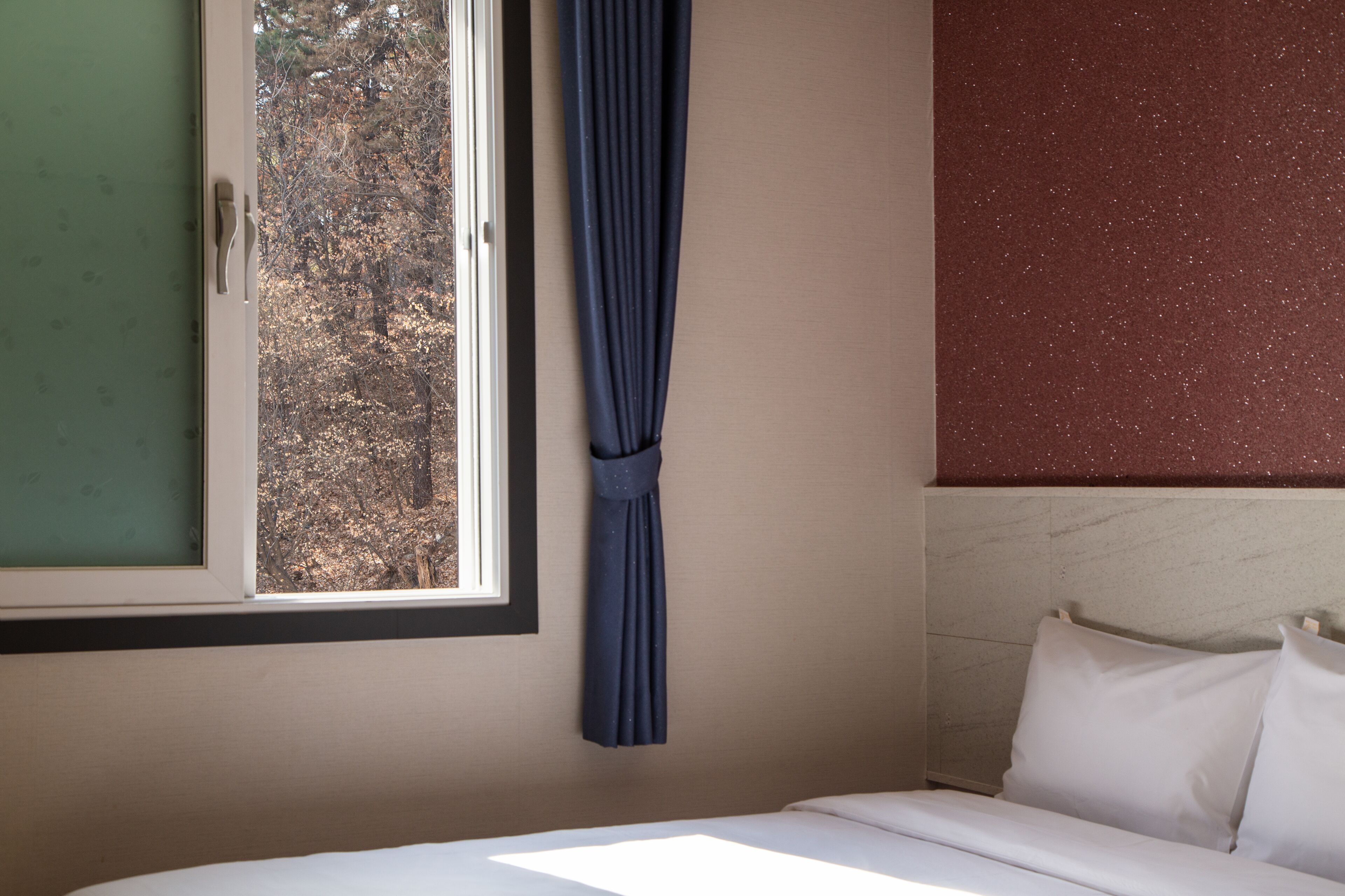 Une chambre d’hôtel avec un lit, une fenêtre avec un rideau et une vue sur les arbres à l’extérieur.