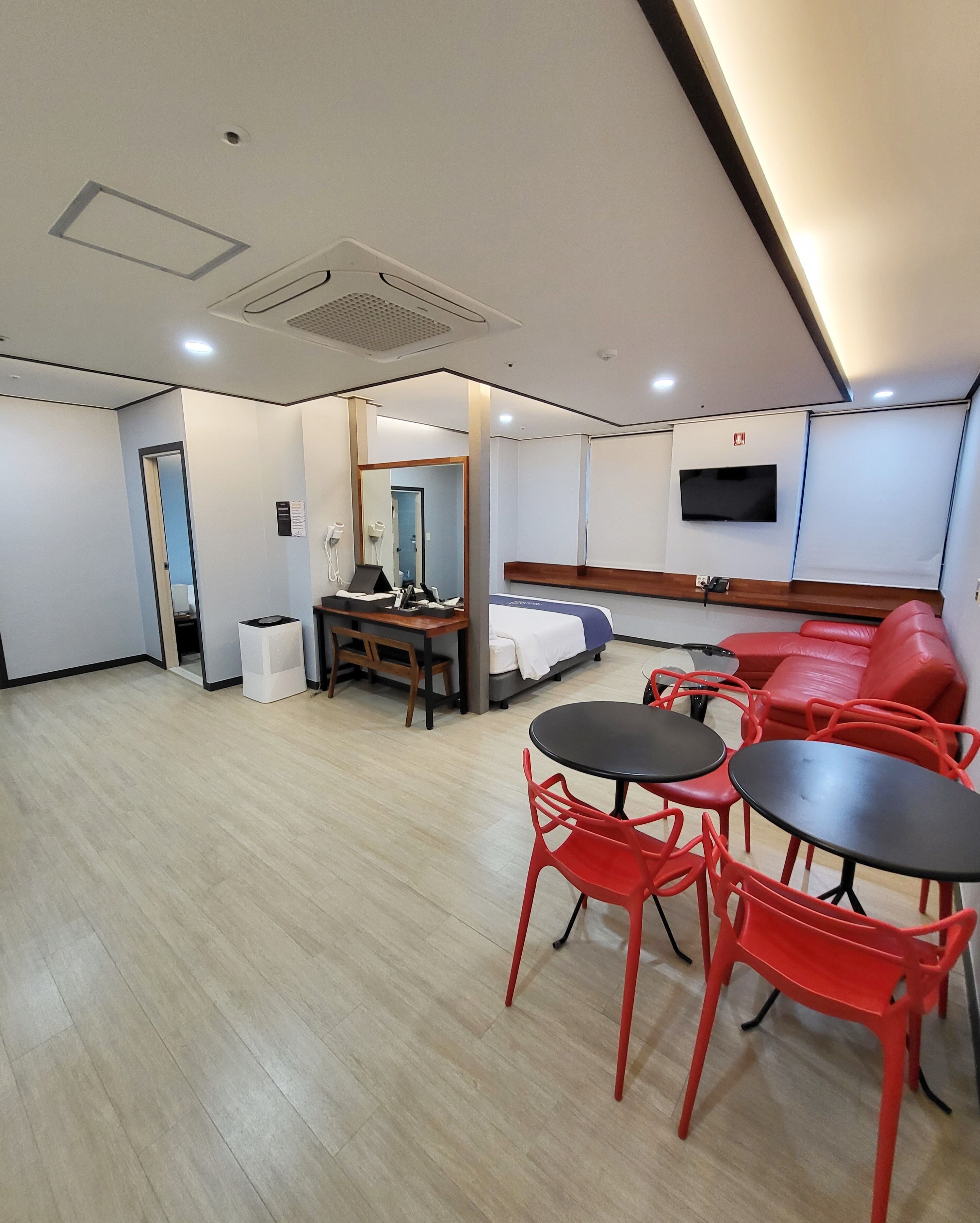 Una habitación de hotel moderna con una cama, un escritorio con una silla, un sofá rojo y un televisor montado en la pared.
