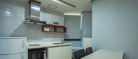 Una cocina compacta equipada con refrigerador, microondas, lavamanos y una mesa de comedor con sillas.