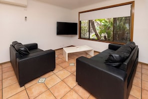 Una stanza con due divani in pelle nera, un tavolino da caffè bianco, una TV a schermo piatto montata a parete e una finestra vista verde.