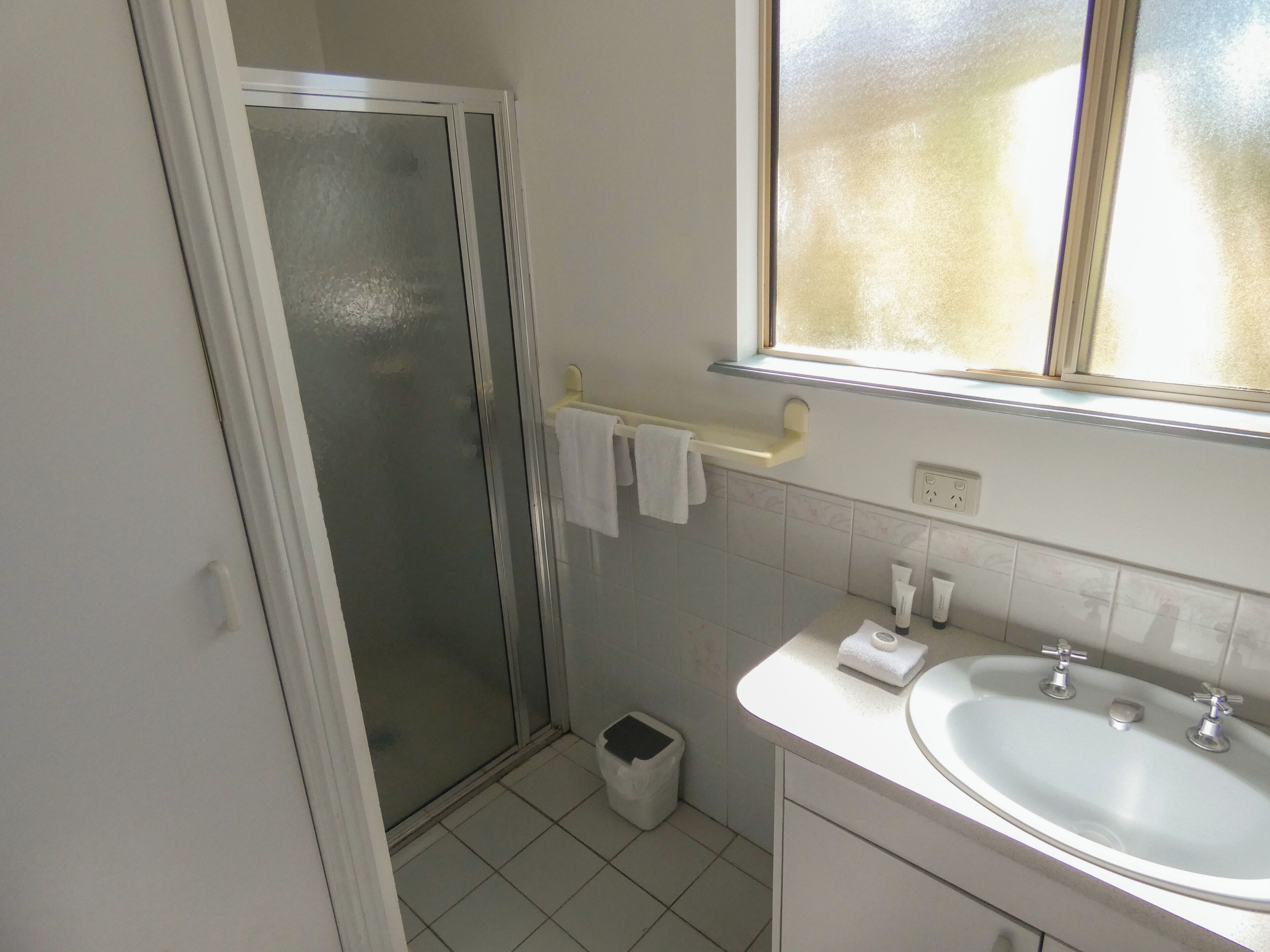 Une salle de bain avec une douche, un lavabo, une fenêtre et un porte-serviettes.