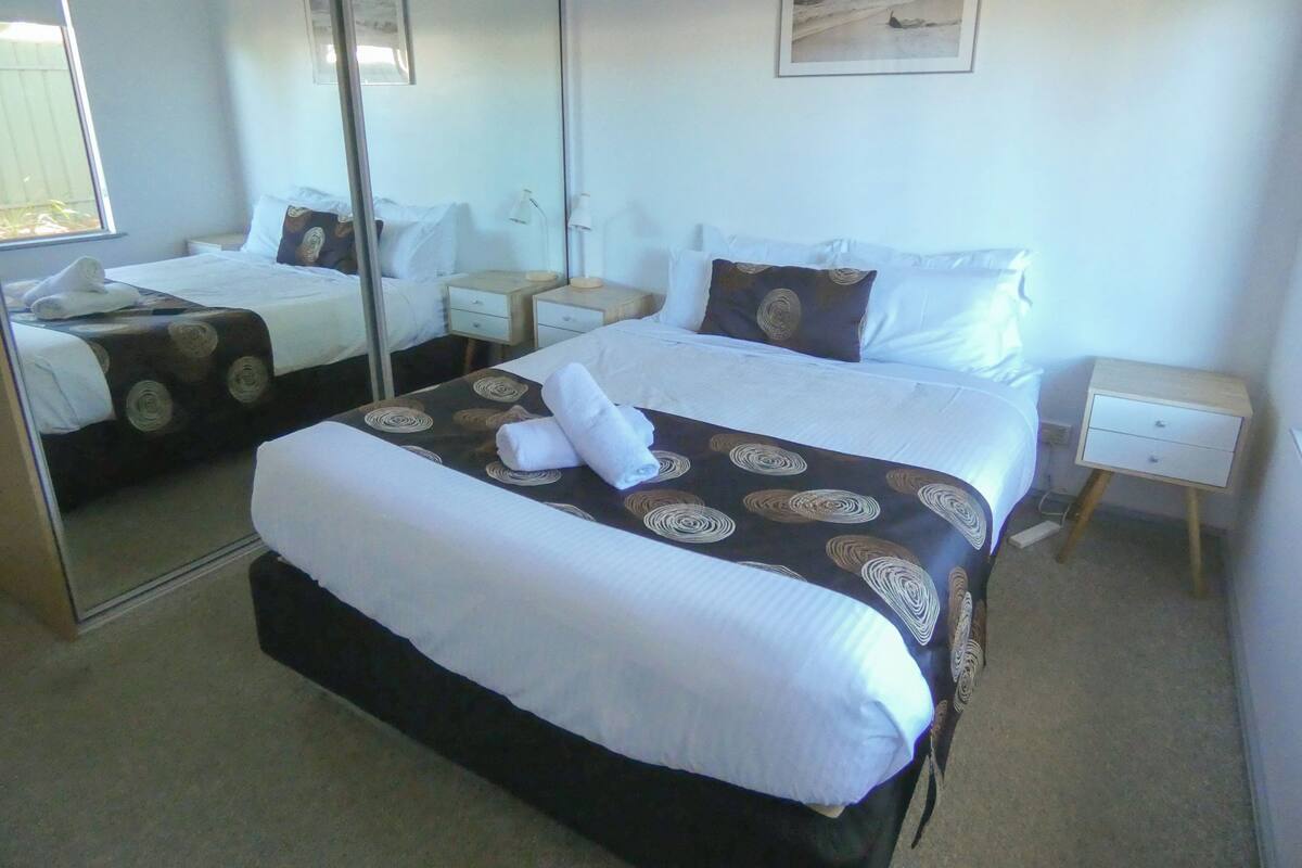 Een hotelkamer met een groot bed, twee nachtkastjes, een spiegel en een schilderij aan de muur.