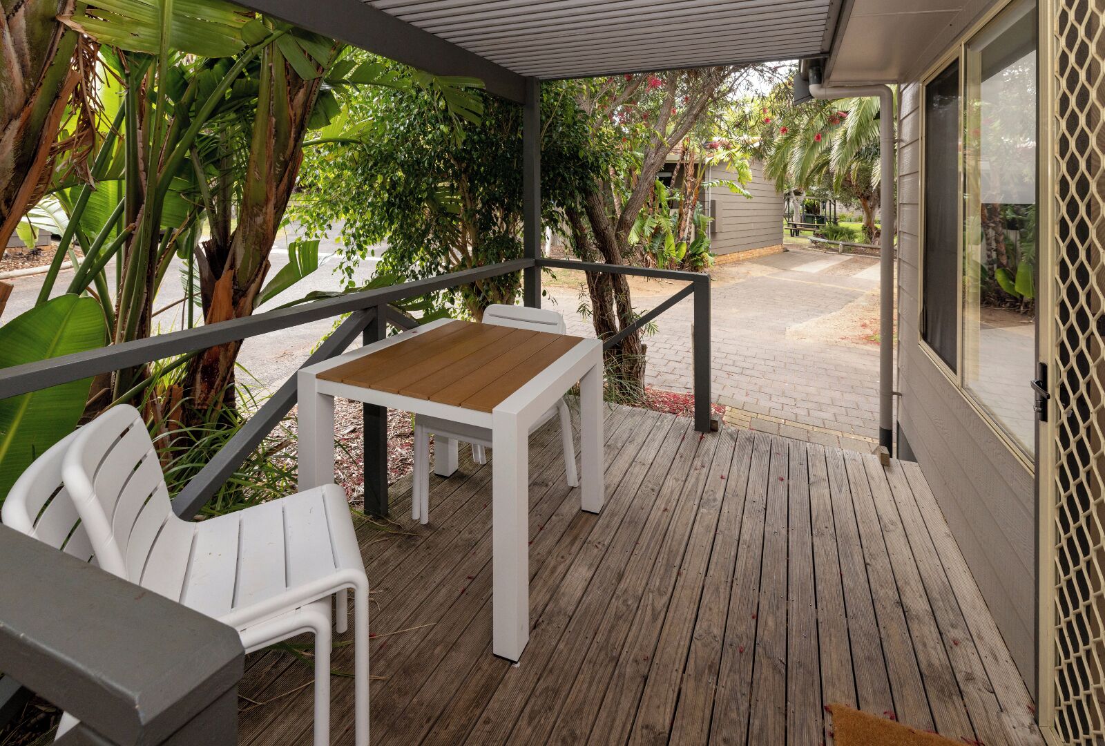 A wooden deck with a table and chairs, surrounded by tropical plants.