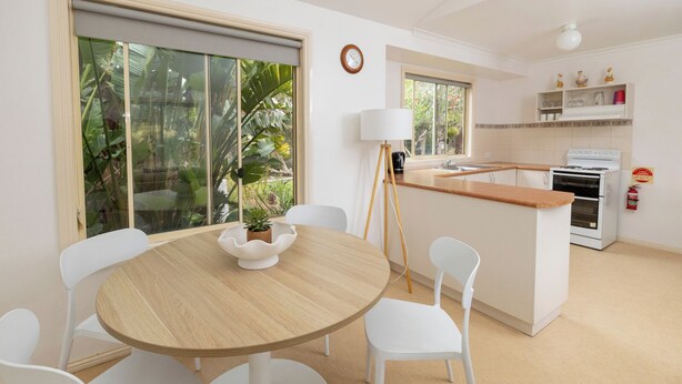 Une cuisine moderne avec un îlot central, des chaises blanches, une table ronde et une vue sur la verdure à l’extérieur.