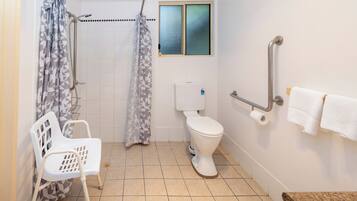 A bathroom with a shower, toilet, grab bar, and a chair.