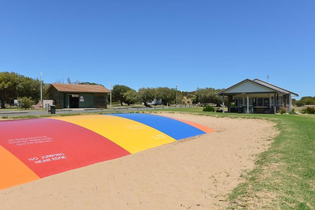 A playground with a colorful safety surface and a small building in the background.