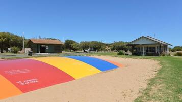 A playground with a colorful safety surface and a small building in the background.