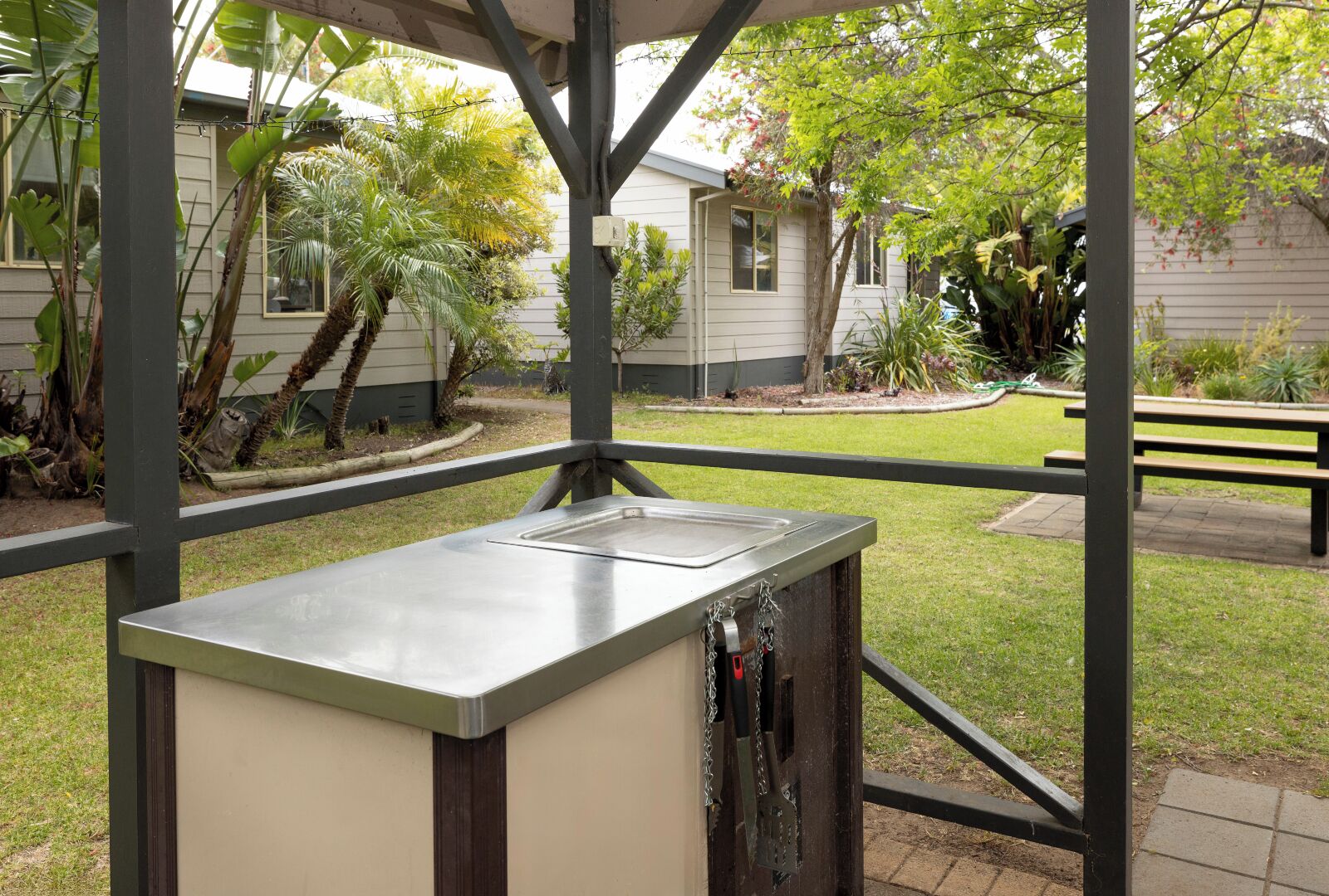 Un espace extérieur abrité, avec une table en métal, un banc et une vue sur une maison et un jardin.