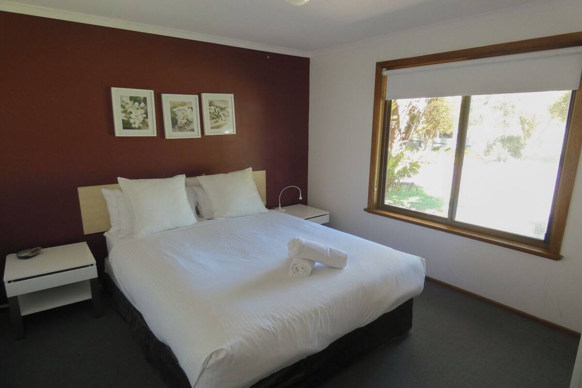 Een hotelkamer met een bed, nachtkastjes, een raam met uitzicht en drie ingelijste foto's aan de muur.