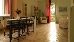 A dining area with a table and chairs, a bookshelf, a white armchair, and a radiator. - Bed & Roses (Montesilvano)