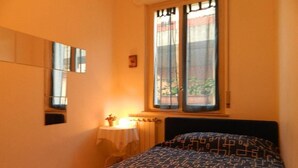 A bedroom with a bed, a window with curtains, a bedside table with a lamp, and a wall-mounted mirror. - Bed & Roses (Montesilvano)