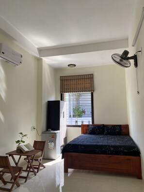A bedroom with a bed, a desk with a chair, a radiator, a window with blinds, and a wall-mounted fan. - Win's Homestay - Hostel (Da Nang)