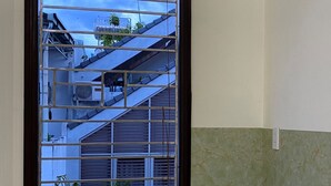 Ein Fenster mit einem Gewebeschirm, Blick auf ein Gebäude mit Satteldach und Klimaanlagen, und eine grüne und beigefarbene Wand.