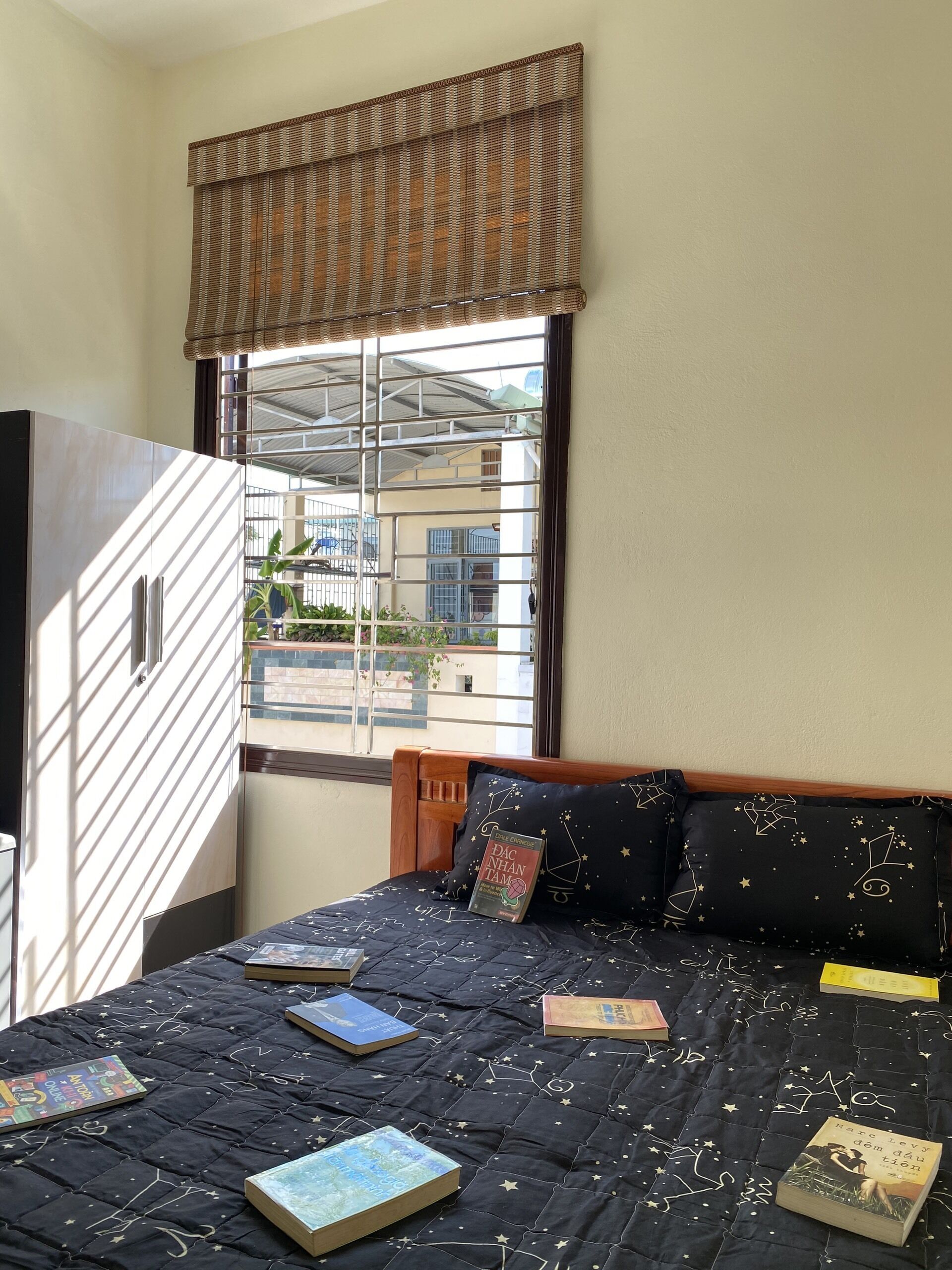 Une chambre à coucher avec un lit, des livres et une fenêtre donnant sur des immeubles.